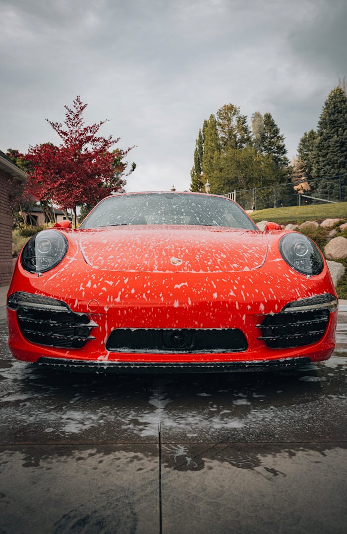 Front view of a luxurious red sports car covered in soap outdoors.